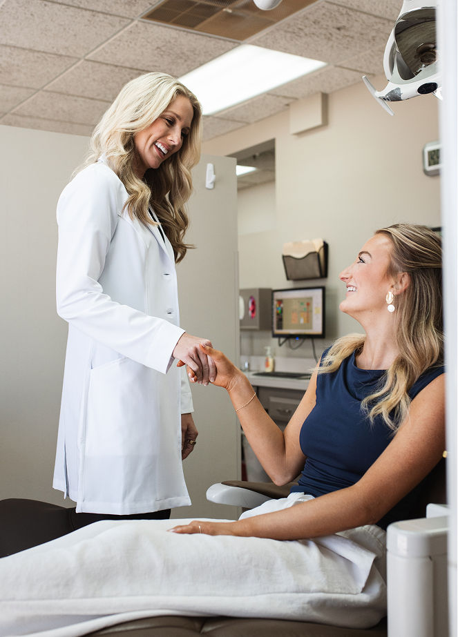 Smiling female doctor in a white coat shakes hands with a seated female patient in a dental clinic, conveying warmth and trust during a consultation.